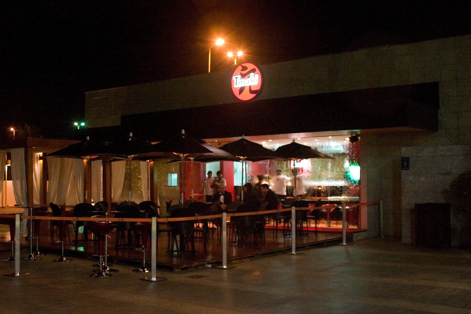Fachada noturna do Tmaki com o logo vermelho aceso